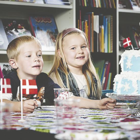 To børn sidder ved et bord med flag og kage.  