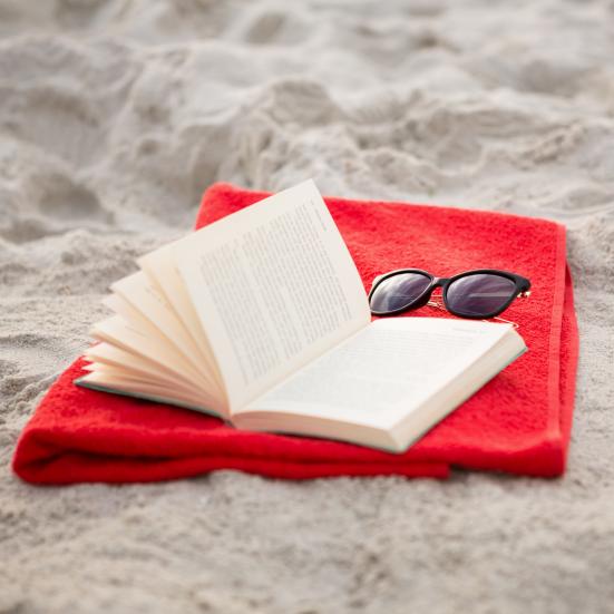 En bog, et håndklæde og solbriller ligger på stranden