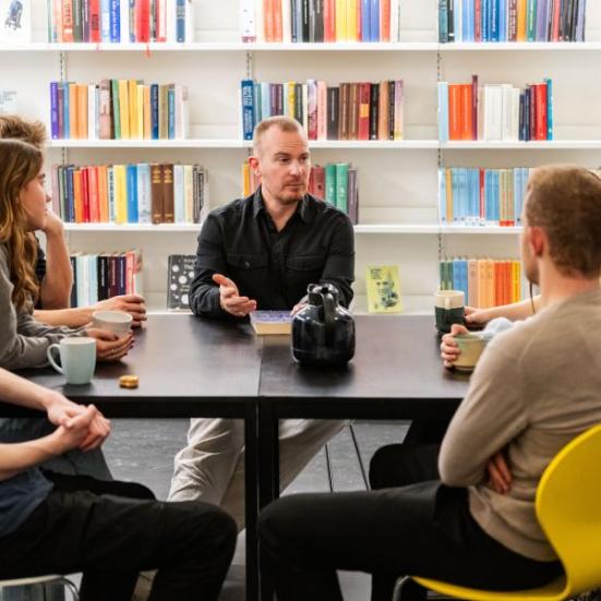 En gruppe mennesker sidder omkring et bord i biblioteket. 