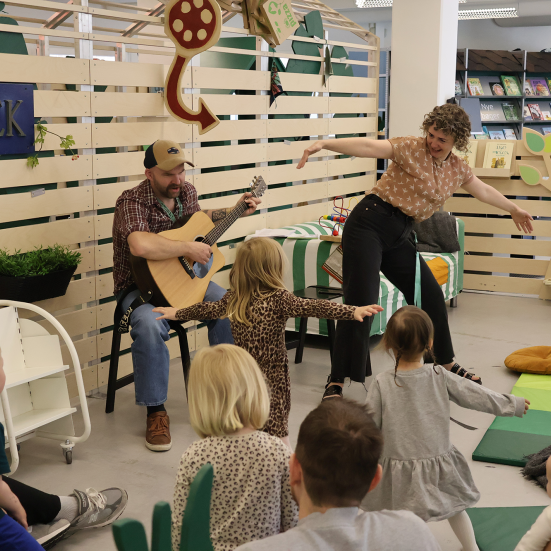 To bibliotekarer underholder med sang for en gruppe børn