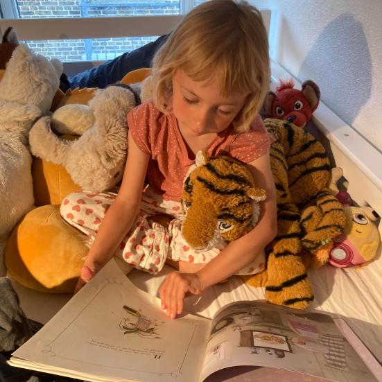Et barn læser i en bog sammen med sin tigerbamse
