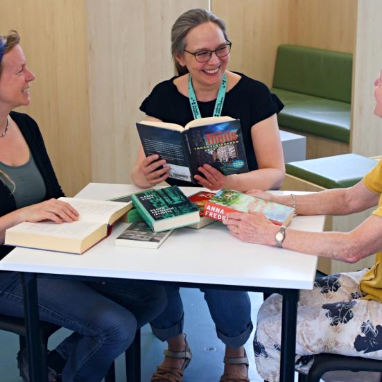 3 kvinder sidder ved et bord. På bordet ligger bøger. Billedet illustrerer at de taler om bøgerne. 