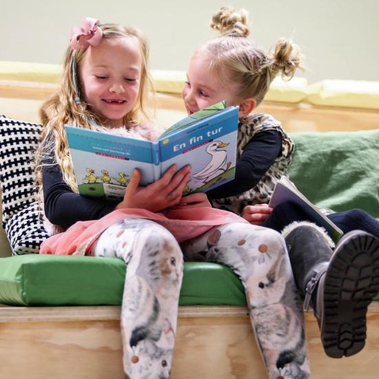 Piger sidder og kigger i en bog. De smiler. 