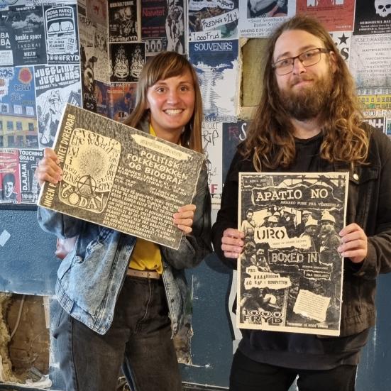 Matilde og Tobias Aske holder en plakat hver foran sig. Man kan se deres ansigter, og at de smiler. Billederne er taget på 1000Fryd, hvor væggene er dækket af plakater.