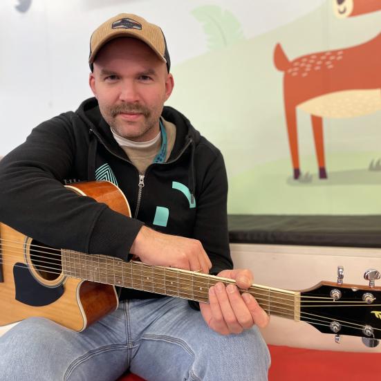 En person sidder i børneafdelingen på Svenstrup bibliotek med sin guitar.