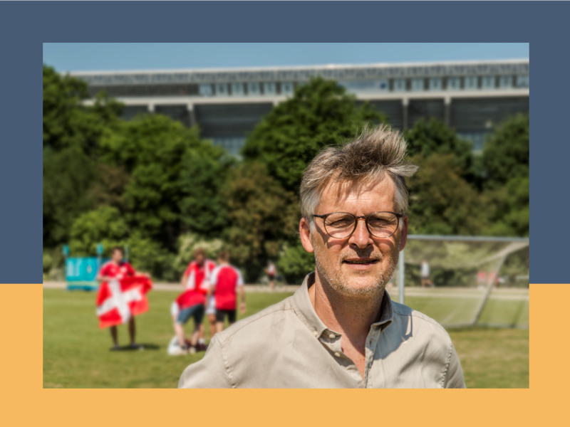 Morten Bruun står på en fodboldbane. I baggrunden står mennesker med danske flag. 