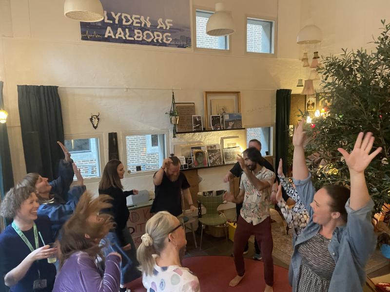 en gruppe mennesker danser i en rundkreds i Folkestuen på Hovedbiblioteket