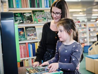 En voksen og et barn står i et bibliotek foran en udlånsautomat