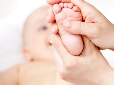 En baby ligger på ryggen og får fodmassage af en voksen. Babyens fod samt den voksnes hænder er i fokus forrest i billedet, resten af babyens krop ses sløret i baggrunden. 