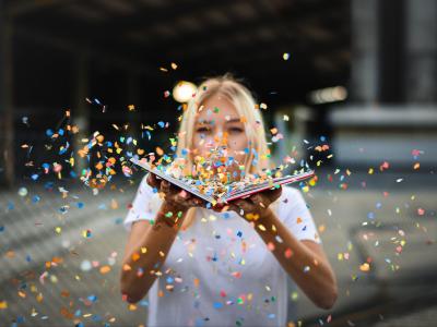 Ung kvinde der puster konfetti udover en bog