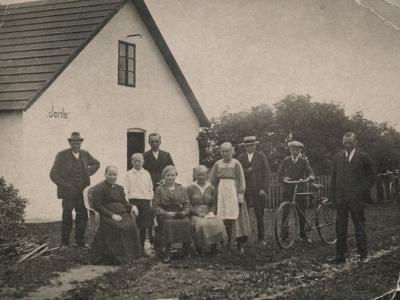 Et ældre foto i sort/hvid af en familie der står foran deres hus. 