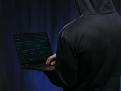 En person står med ryggen til og holder en bærbar computer. Billedet er mørkt. 