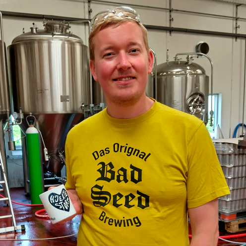 Frederik fra Bad Seed Brewing står foran ølkedler med en "Hjertestorm-kop" i hånden.