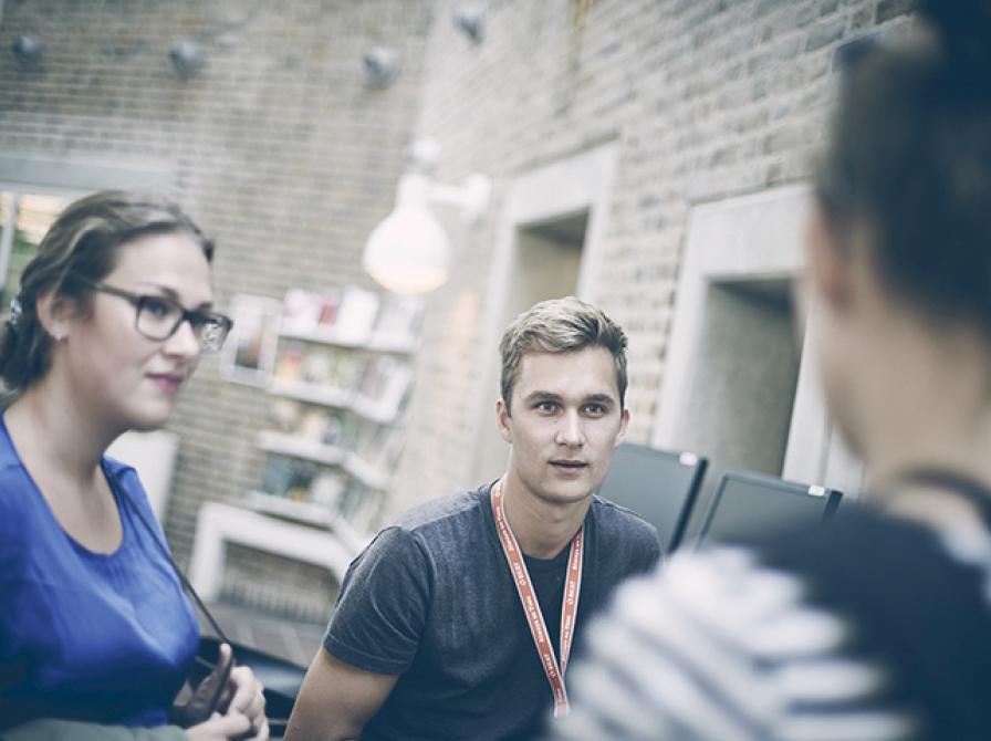 Tre mennesker står og taler sammen i biblioteksrummet