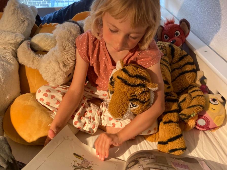 Et barn læser i en bog sammen med sin tigerbamse