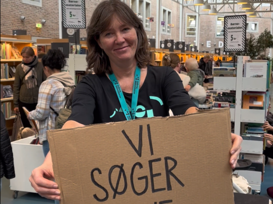 En person står med et skilt med teksten "Vi søger nye..." på