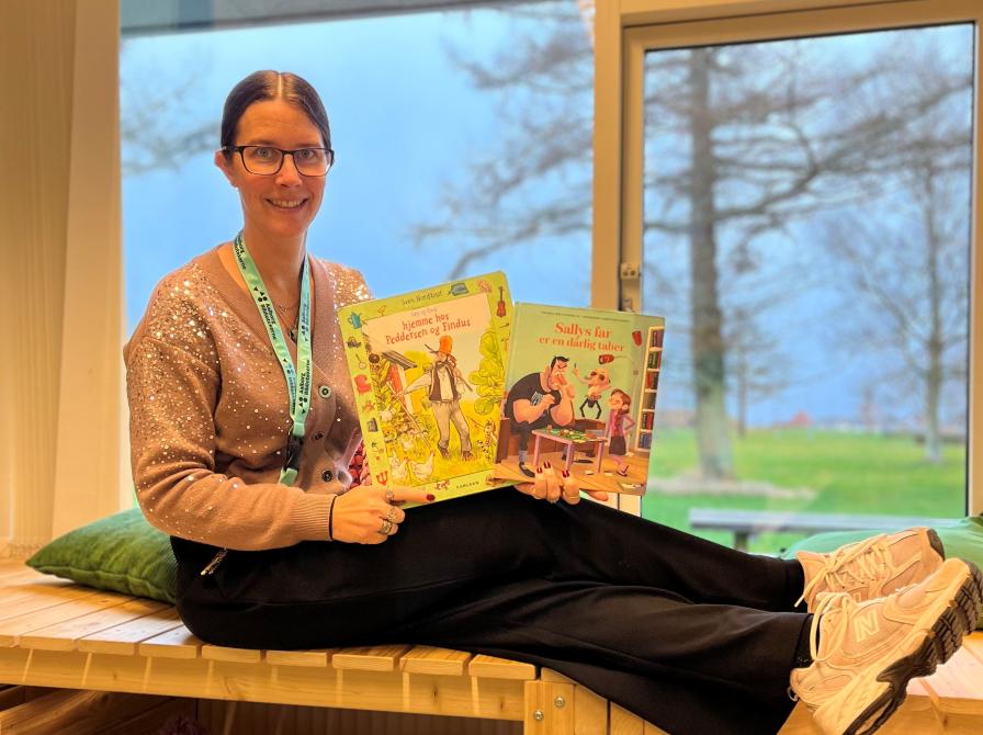 Line sidder på en træbænk på Hals bibliotek. I hænderne har hun to af de omtalte bøger.