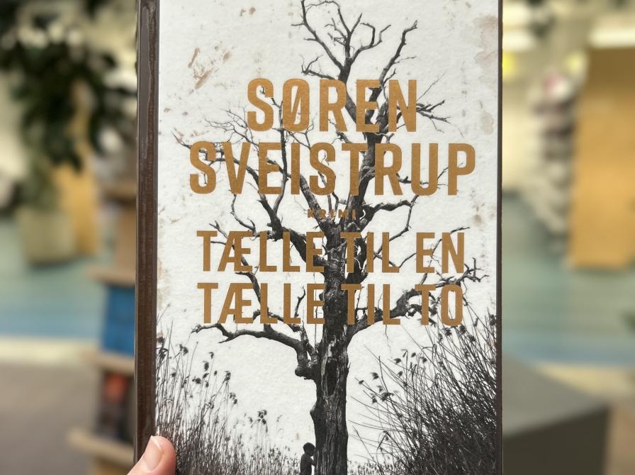 Et close uo foto af bogen "Tælle til en, tælle til to" af Søren Sveistrup. Baggrunden, som er let sløret, viser biblioteksrummet.